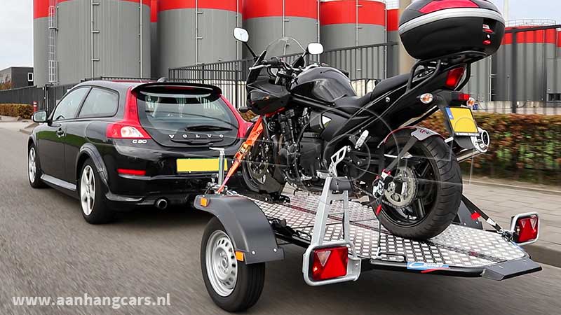Rijdende auto met aangekoppelde Cochet Uno verlaagbare motortrailer waarop één motor staat