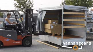 Vorkheftruck plaatst een pallet met dozen in de laadbak van een Eduard plateauwagen die is voorzien van een huif