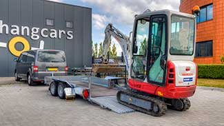 Een kleine graafmachine wordt de laadbak van een Humbaur Senko zakbare machinetransporter in gereden.