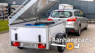 Een beladen Power Trailer bagagewagen met geopend deksel achter een grijze stationwagen